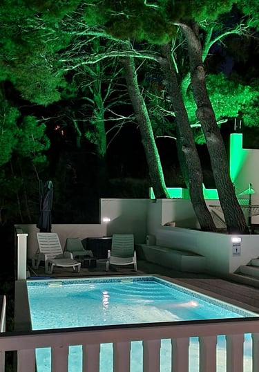 The photograph depicts an illuminated pool and part of the courtyard of Lokva Rogoznica's house.