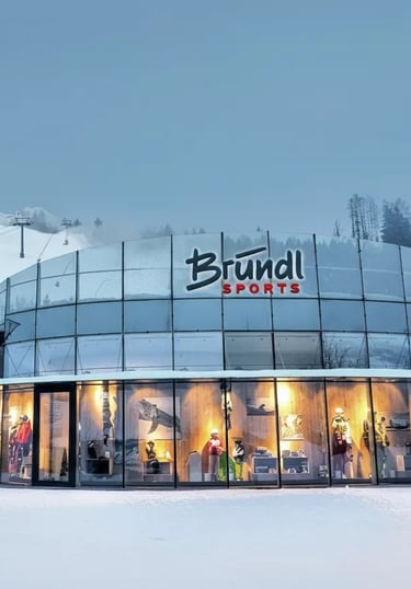The modern, illuminated glass exterior of a Bründl Sports shop in Zell am See, showcasing winter spo
