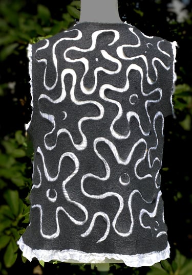 Handmade black nuno felted wool vest with white abstract floral swirl patterns and ruffled hem.