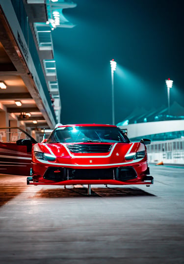 Red Ferrari racing car on a race track at night under bright stadium lights.
