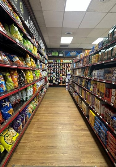Aisle in Round Hill Market with shelves stocked with various snacks, including chips and crackers, under bright lights.