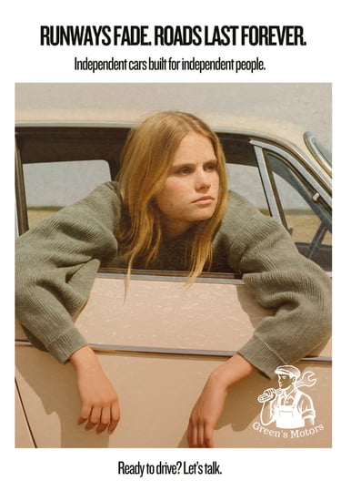 A young blonde woman rests her arms out of the passenger window of a cream-colored vintage car. She wears oversized knitwear 