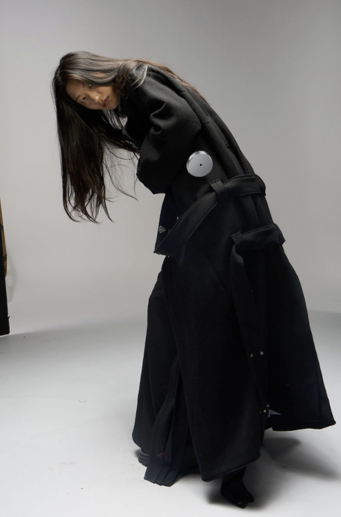 A fashion model wearing an oversized black designer wool trench coat posing in a studio.