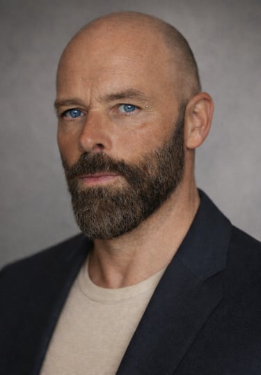 Professional portrait of Damon with blue eyes and a groomed beard wearing a dark blazer.