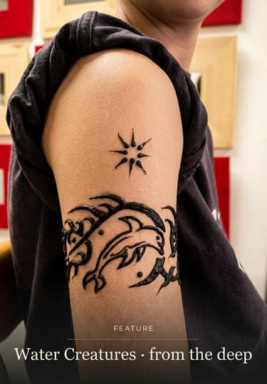 A black ink arm tattoo featuring a dolphin jumping through waves with a sun symbol above it.