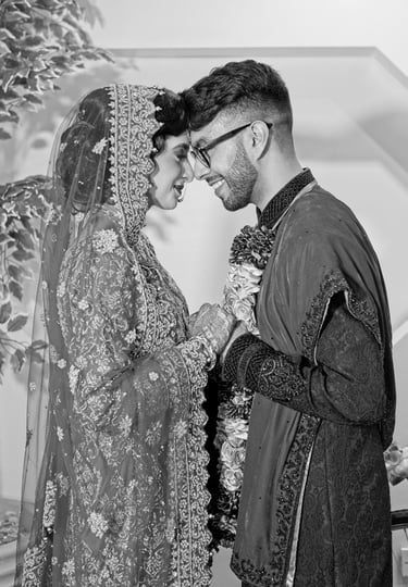 black and white photo of asian bride and groom wearing traditional wedding clothes, holding hands and foreheads touching 