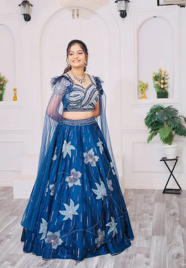 “A bride standing in a bright white studio, wearing a royal blue floral embroidered lehenga with 