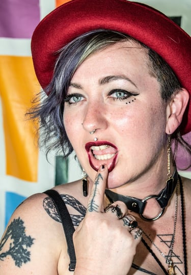 portrait of a girl dressed in a punk style with purple hair with finger on bottom lip daintily