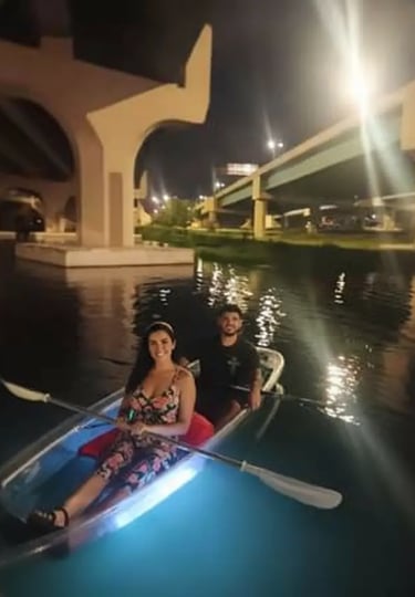 Couple enjoying a romantic date night in a clear kayak with blue glow lights during a bioluminescent