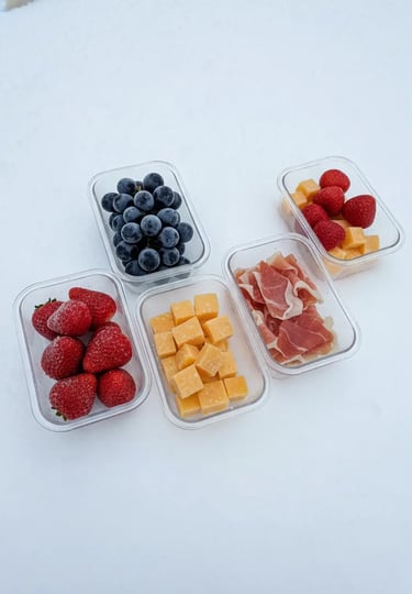 Prepped snack containers with strawberries, blueberries, cheese cubes, and prosciutto organized on t