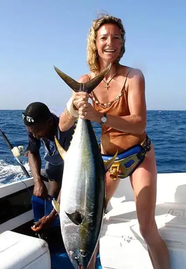 woman on a fishing boat in Zanzibar with a local expert fisherman, lifting a large kingfish during a fishing tour experience