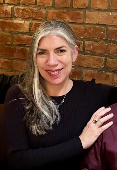 Portrait of poet Sheena Powell smiling, standing against a brick wall