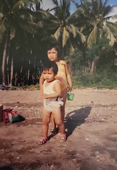 My sister and I on the beach, tropical foliage in the background.