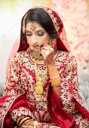candid portrait of asian bride wearing traditional red dress with gold embroidery, her hands full of henna, looking down