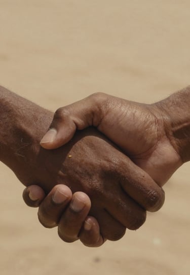 A candid close-up of hands held tightly, warm earthy brown skin tones against a soft sand fabric background, cinematic photography style.