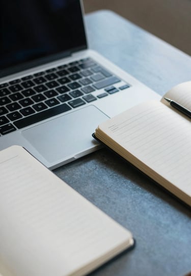A detail shot of a laptop keyboard and a designer's notebook on a steel blue desk in a quiet North American / US workspace.