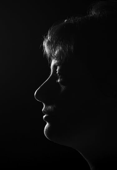 Dramatic black and white profile silhouette of a person's face against a dark background.