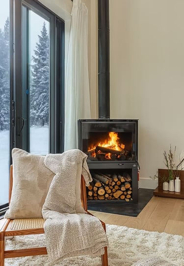 Cozy warmth meets nature's embrace. Crackling fire, plush textures beckon. Large windows frame green