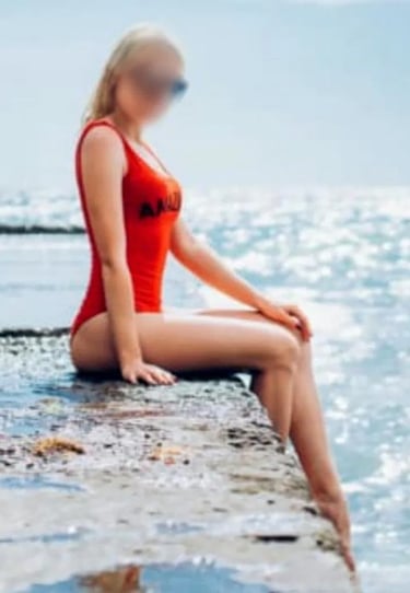 Ana sentada junto al mar en bañador rojo, mostrando su silueta perfecta y su piel dorada.