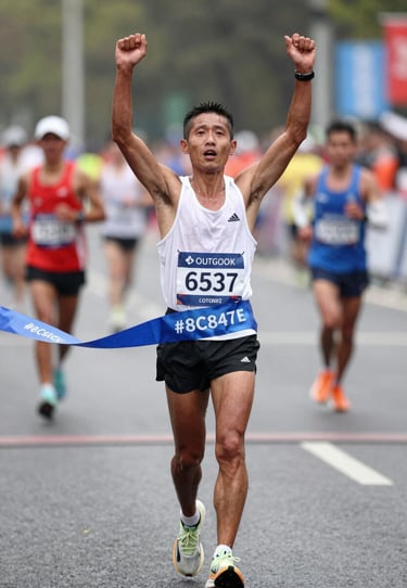 Emotional shot of a marathon runner crossing the finish line, arms raised, authentic victory, natural lighting, #8C847E tones.
