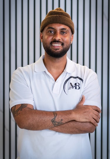 well lit Portrait photo of Maji, Co-owner of MB Barbers Manchester, posing with a smile and his arms crossed