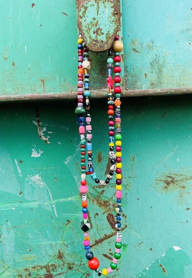 Handmade colorful beaded necklaces hanging on a rustic teal metal surface.
