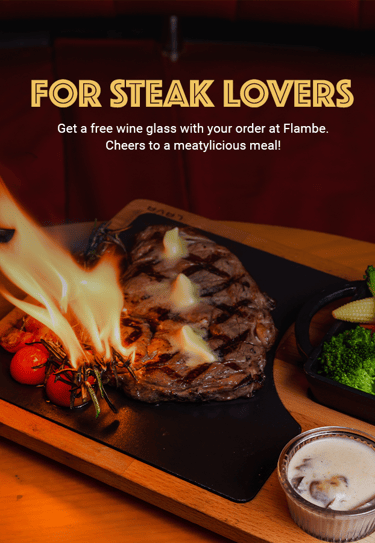 Flaming steak served on a wooden board with grilled vegetables and sauce. Text promotes a free wine.