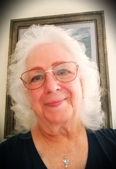 A lady with glasses and a bird necklace on.
