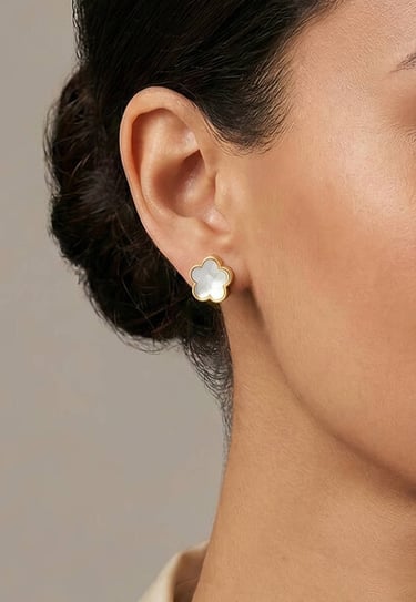 Una mujer lleva un pendiente de botón dorado con forma de flor e incrustación de nácar blanco.