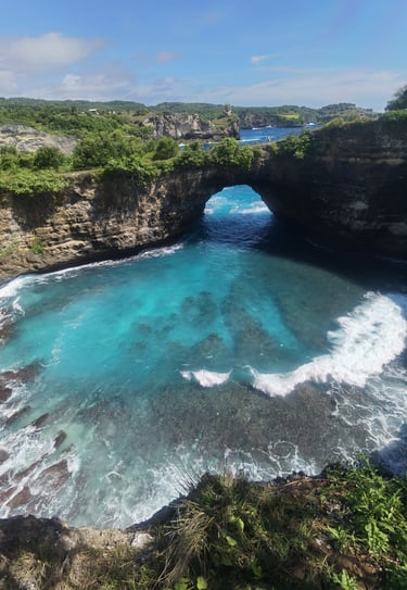 Scenic view of Broken Beach in Nusa Penida, Bali, featuring a natural limestone arch over turquoise ocean water.