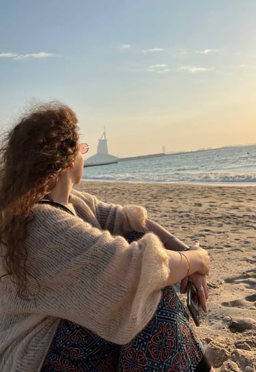 a woman sitting on a beach with a sailboat in the background