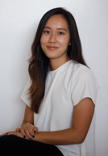 Ashley Sojin Kim sits with her hands crossed in her lap, wearing a white shirt and black pants.