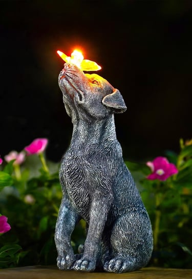 Solar powered dog garden statue with a glowing butterfly on its nose among pink flowers.