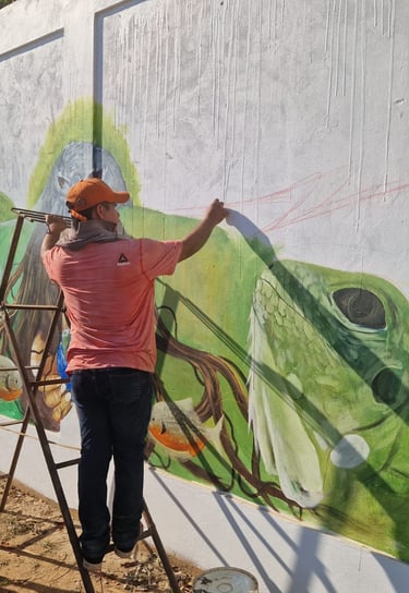 An artist on a ladder painting a colorful street mural at Centro Recreacional Mokanranko