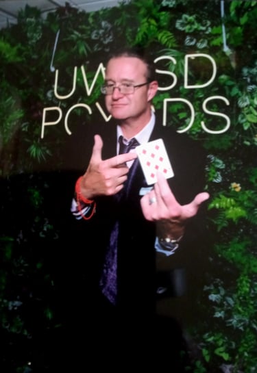 Professional magician in a suit performing a card trick with a nine of diamonds at an event.