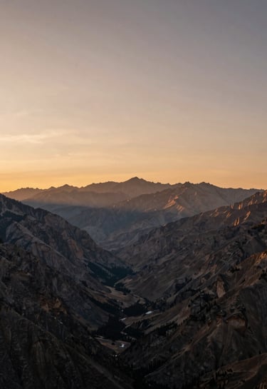 A wide-angle sunrise shot over a North American mountain valley, with the peaks glowing in a muted bronze light. The composition is balanced and simple, showcasing the vast beauty of nature in a professional photography style.