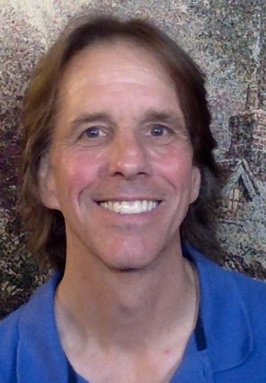 Smiling middle-aged man with brown hair wearing a blue polo shirt in a headshot portrait.