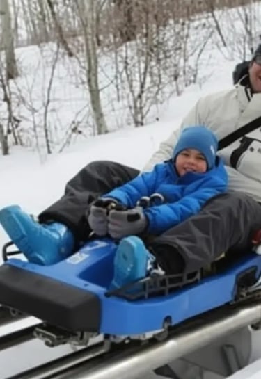 Close-up of a young boy in a blue jacket and beanie enjoying a mountain coaster ride on a snowy trac