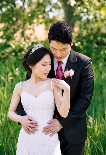 A bride and groom in a lace wedding dress and black tuxedo posing for a romantic outdoor wedding portrait.
