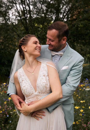 A happy bride and groom embrace in a wildflower garden during their summer wedding ceremony.