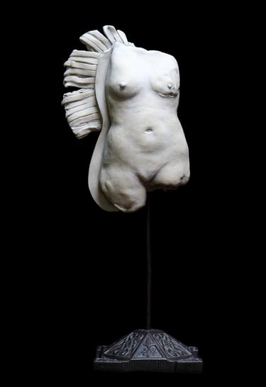 Small ceramic fragment of a nude female figure with a disfigured breast and bedraggled, wing-like fringe.