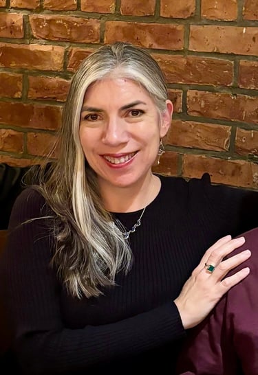 Portrait of poet Sheena Powell smiling, standing against a brick wall