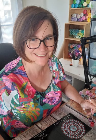 a woman sitting at a table painting dot mandala