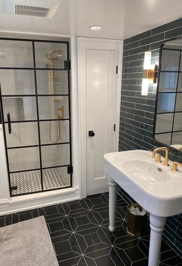 Custom basement shower with glass door, black frame, gold hardware and contemporary freestanding sin