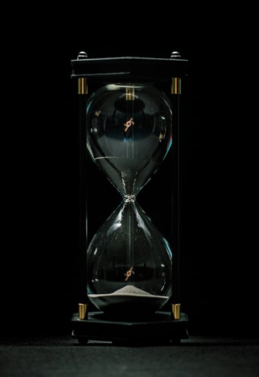 Elegant glass hourglass with white sand flowing against a dark black background.