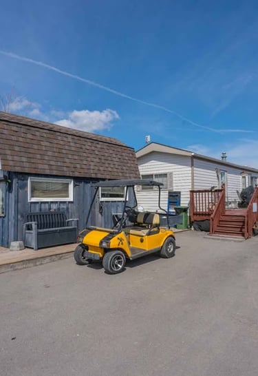 Yellow golf cart parked in front of a blue wooden shed and mobile home with a deck.