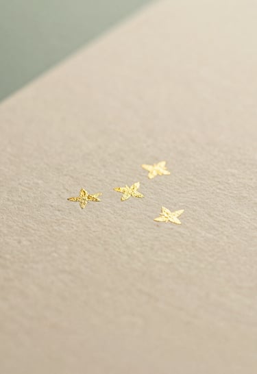 Macro close-up of delicate gold foil details on a textured cream paper, soft golden-hour light, shallow depth of field.