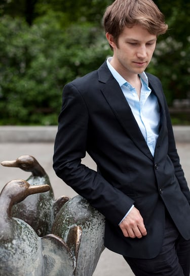 A man in a suit leaning on a fountain in a park.