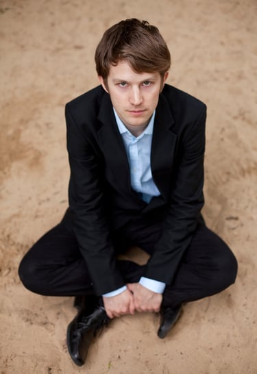 Tyson Naylor sitting on sand wearing a suit.