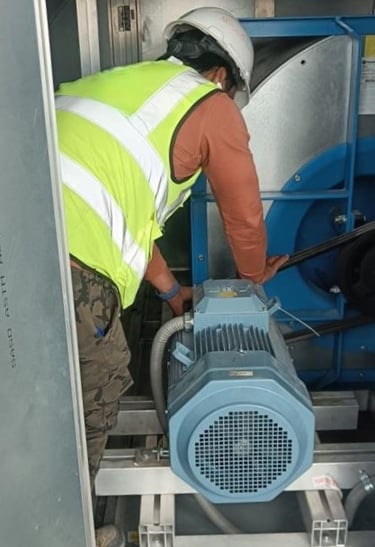 An HVAC technician performing maintenance on a large industrial air handling unit motor.